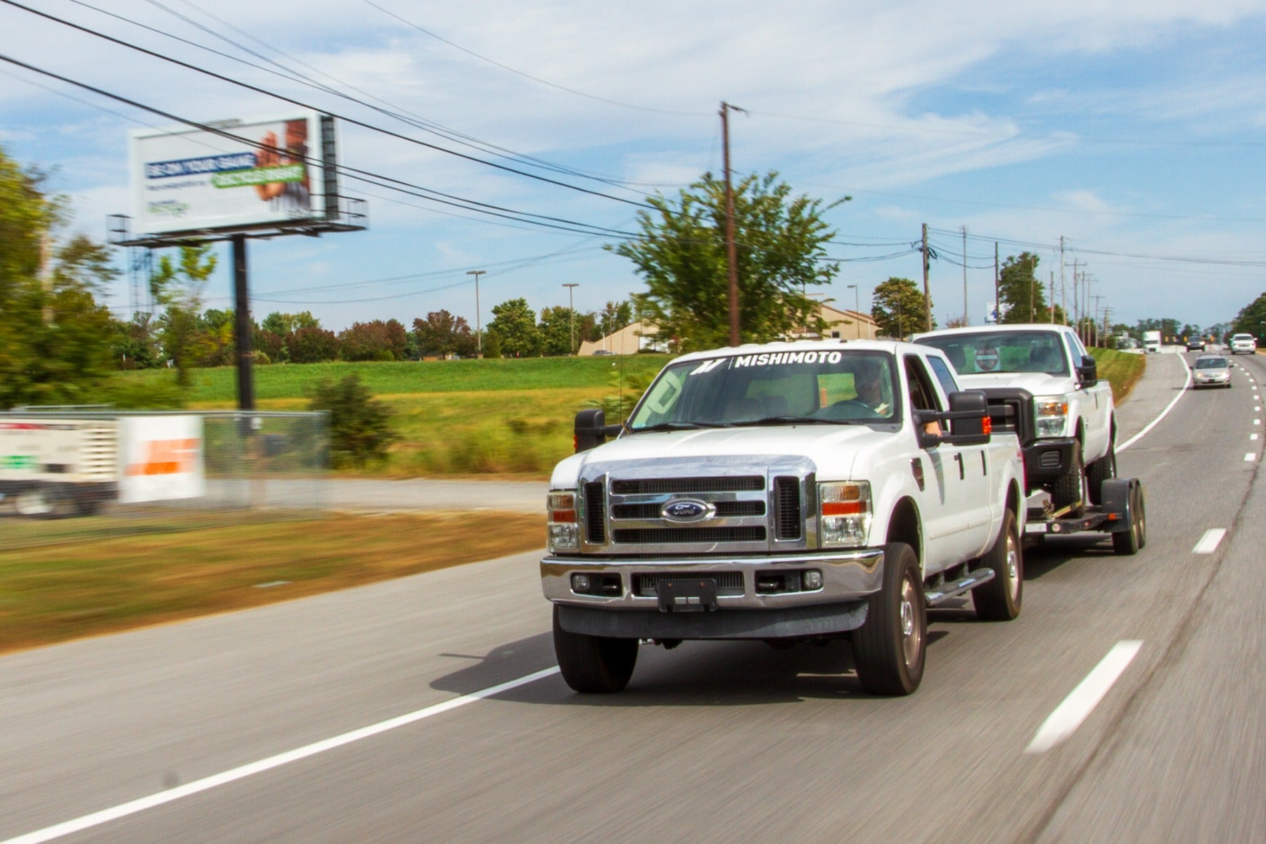 Ford truck towing another Ford truck with a Mishimoto sticker on the highway.